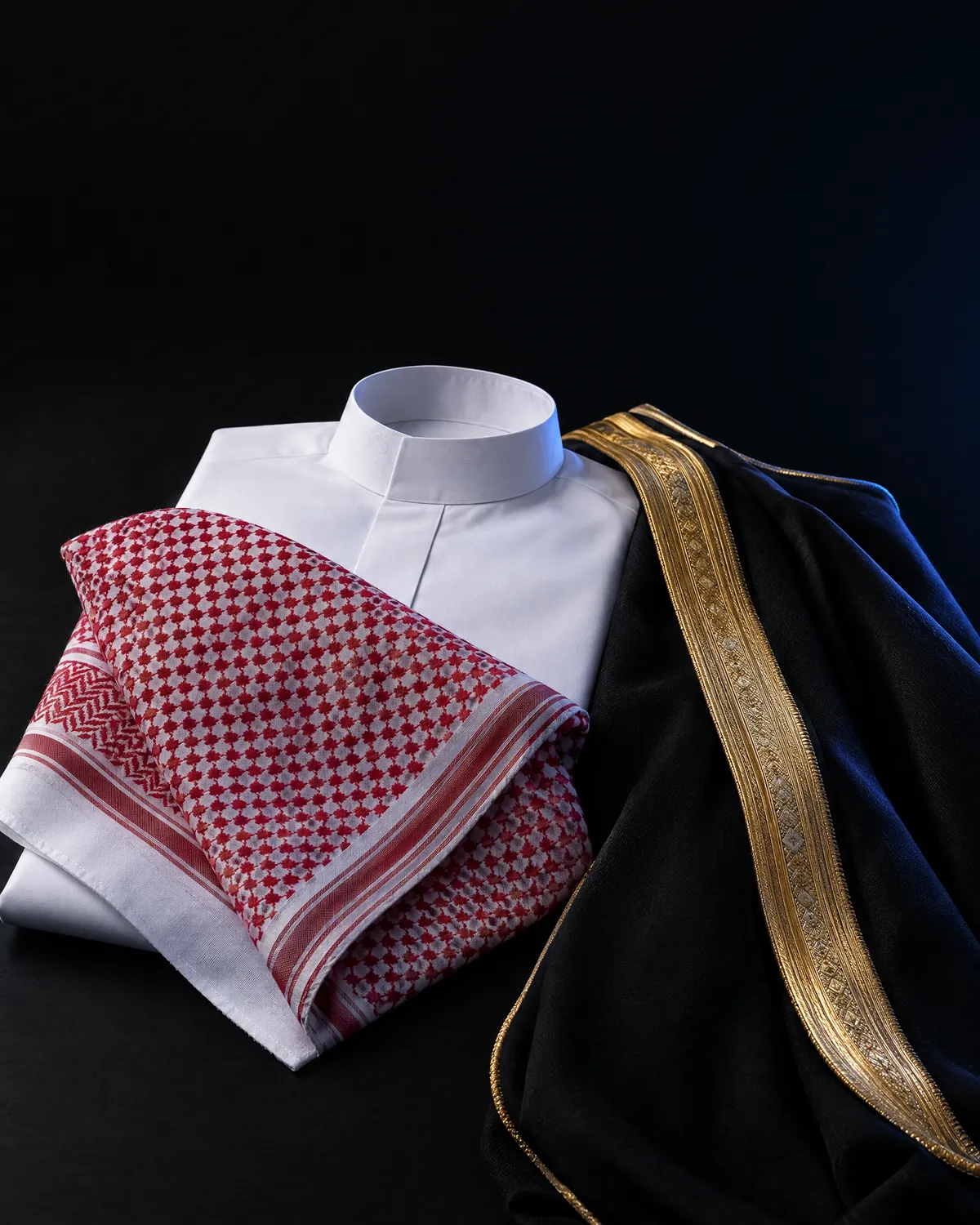 ثوب أبيض مكوي وشماغ أحمر مطوي وطرف بشت أسود بتطريز ذهبي